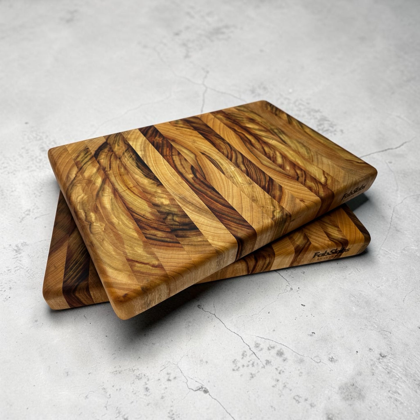 Two Fab Slabs Online Store premium hardwood chopping boards stacked on a grey concrete surface with unique wood grain.